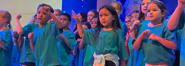 kids in bright teal tee shirts sing during Vacation Bible School