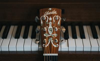 Neck of guitar resting against piano keyboard