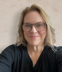 blonde woman wearing glasses and a black top smiles at the camera