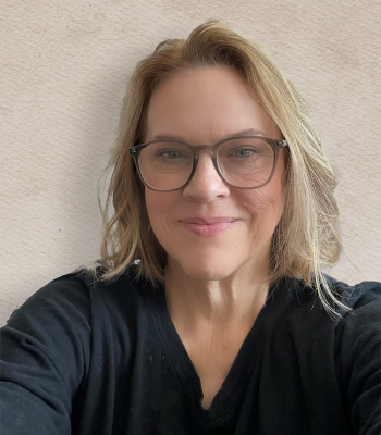 blonde woman wearing glasses and a black top smiles at the camera