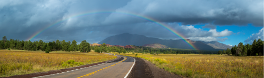 open road with blue sky and rainbow ahead