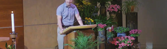 Joe Hill delivers sermon from ambo surrounded by spring flowers